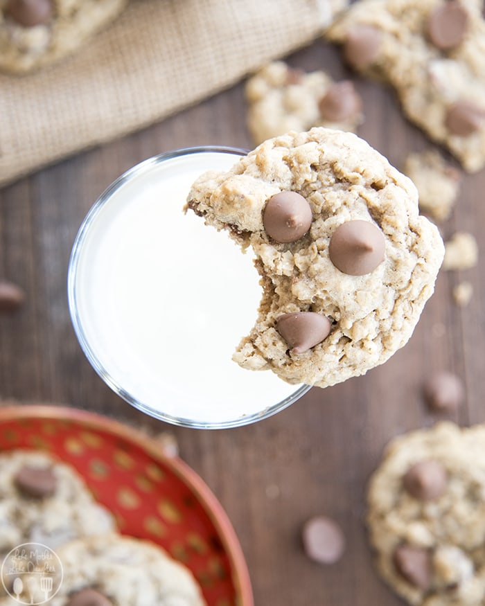 An oatmeal cookie on a glass of milk with a bite out of the cookie.