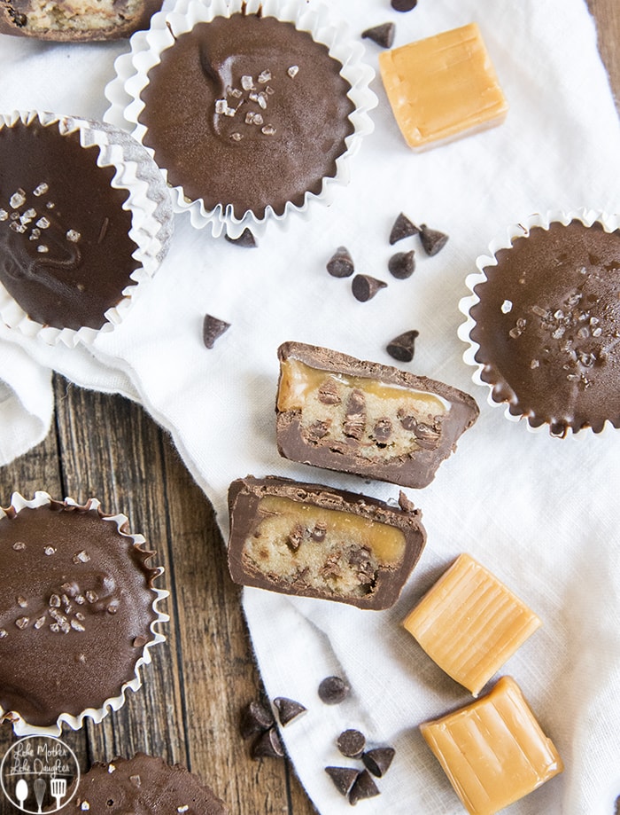 A cookie dough and caramel candy cup cut in half showing the chocolate cup with caramel and cookie dough in the middle. 