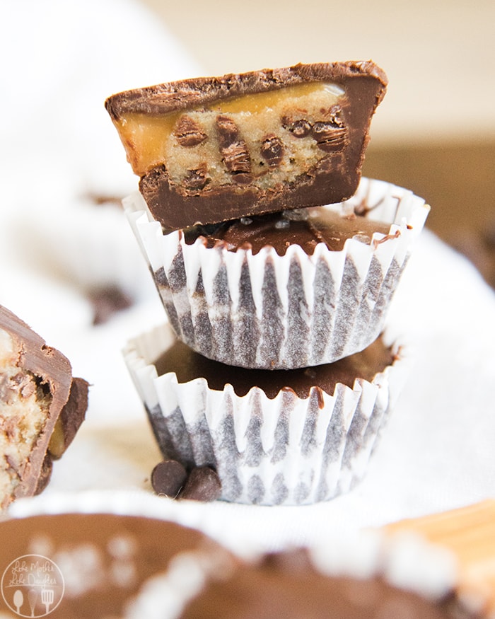 A stack of cookie dough stuffed chocolate cups with the top one cut in half and showing the middle. 