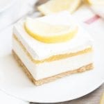 A piece of no bake cheesecake topped with lemon curd, whipped cream, and a lemon slice.