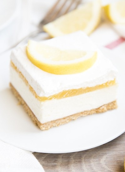 A piece of no bake cheesecake topped with lemon curd, whipped cream, and a lemon slice.