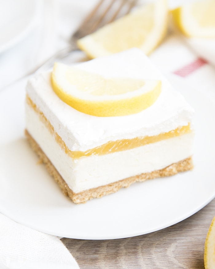 A piece of no bake cheesecake topped with lemon curd, whipped cream, and a lemon slice.