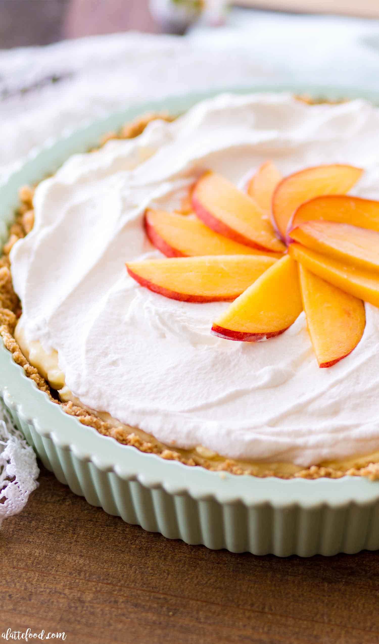 A no bake peach pie topped with whipped cream and peach slices in a tart pan. 