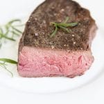 A sous vide steak on a plate topped with fresh rosemary.