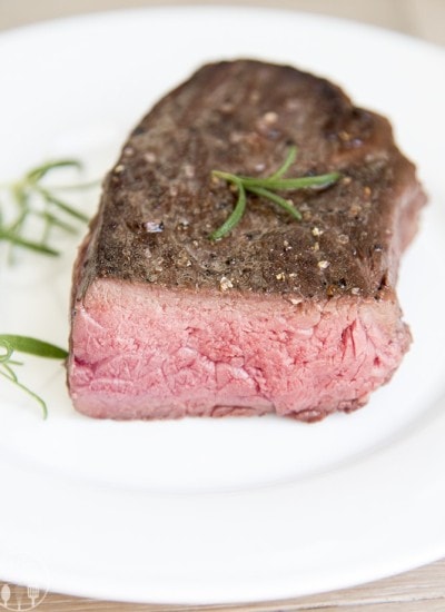 A sous vide steak on a plate topped with fresh rosemary.