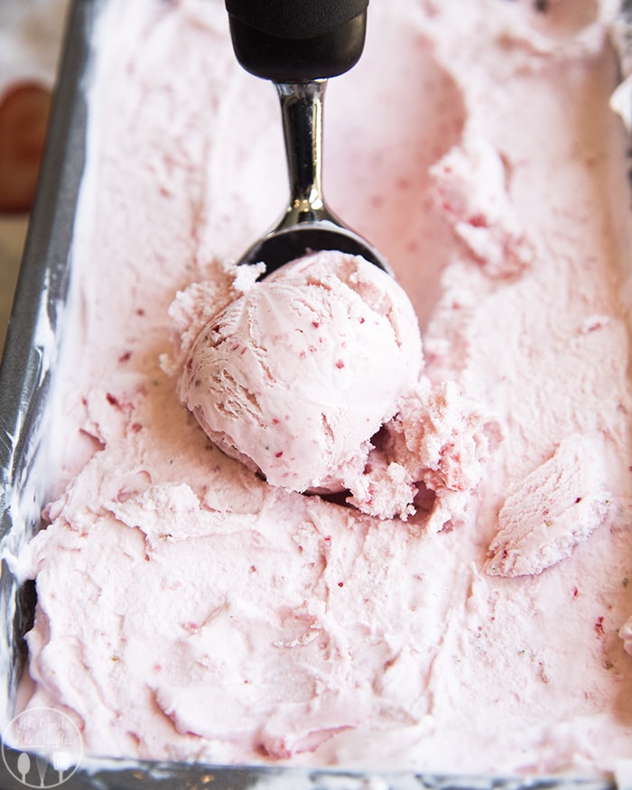 A pan full of strawberry ice cream with an ice cream scoop, scooping ice cream out.