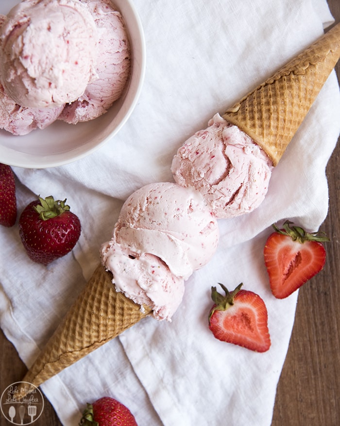 Two strawberry ice cream cones with the ice cream of the cones touching laying down on a white cloth, and the cones facing the opposite directions.