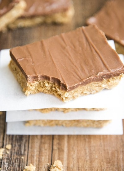 A stack of peanut butter bars with chocolate topping and a bite taken out of the top one.