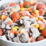 A bowl of halloween muddy buddies with candy corn, reeses pieces, and candy pumpkins.