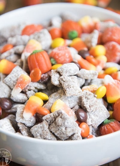 A bowl of halloween muddy buddies with candy corn, reeses pieces, and candy pumpkins.