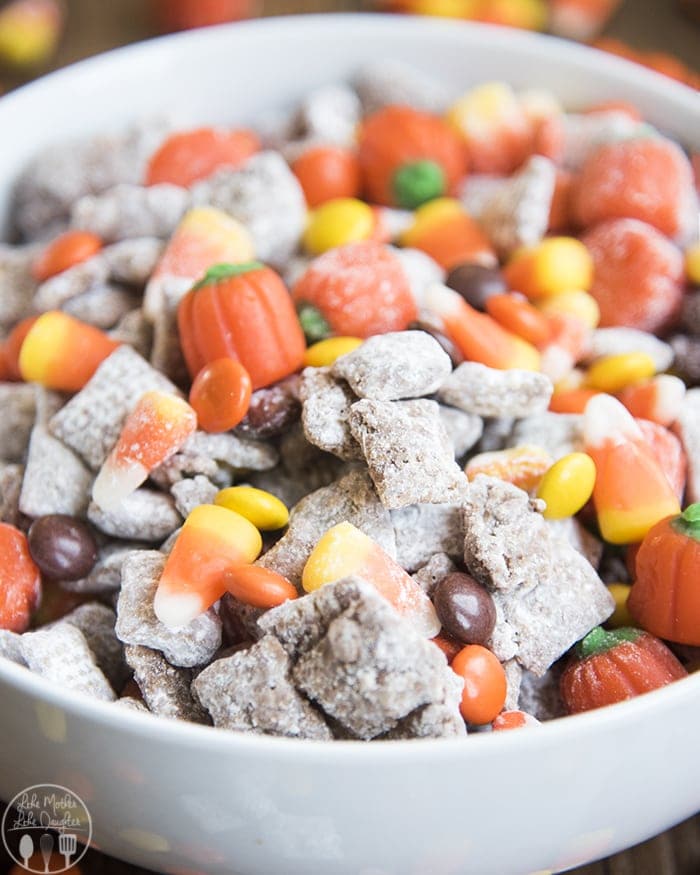 A bowl of halloween muddy buddies with candy corn, reeses pieces, and candy pumpkins.