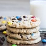 A stack of 4 monster cookies with a glass of milk behind it.