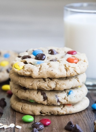 A stack of 4 monster cookies with a glass of milk behind it.