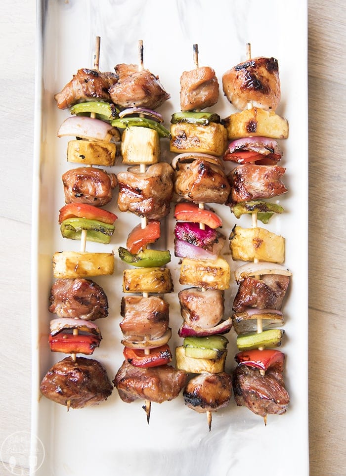 Four kabobs covered in pieces of pork, red bell pepper, red onion, pineapple, and green bell pepper.