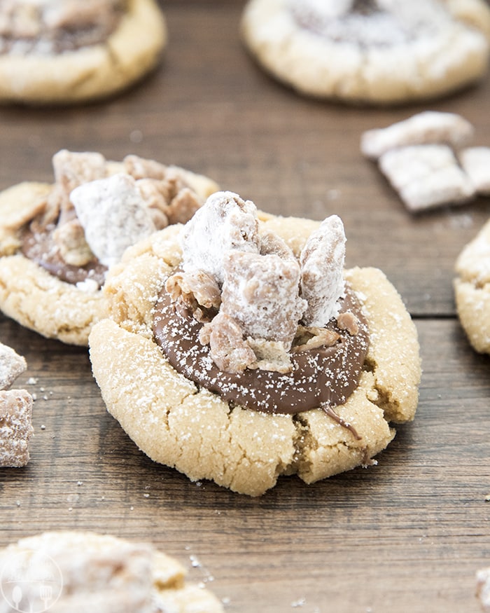 Two peanut butter muddy buddy cookies on a wooden board.