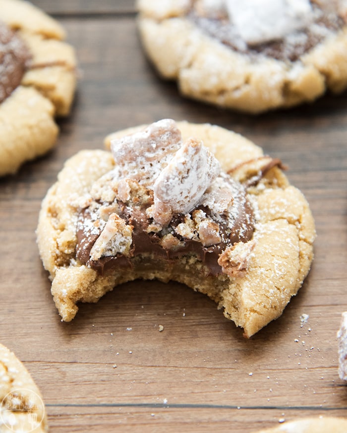A peanut butter cookie with chocolate and muddy buddy on top with a bite out of it.