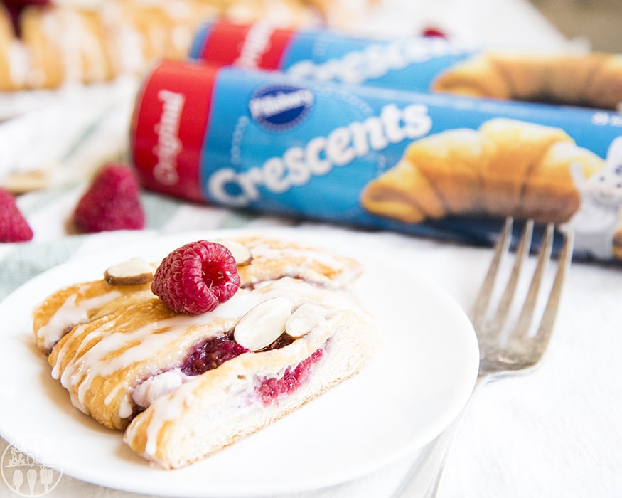 A slice of a raspberry cream cheese pastry on a plate with two cans of crescent rolls behind it.