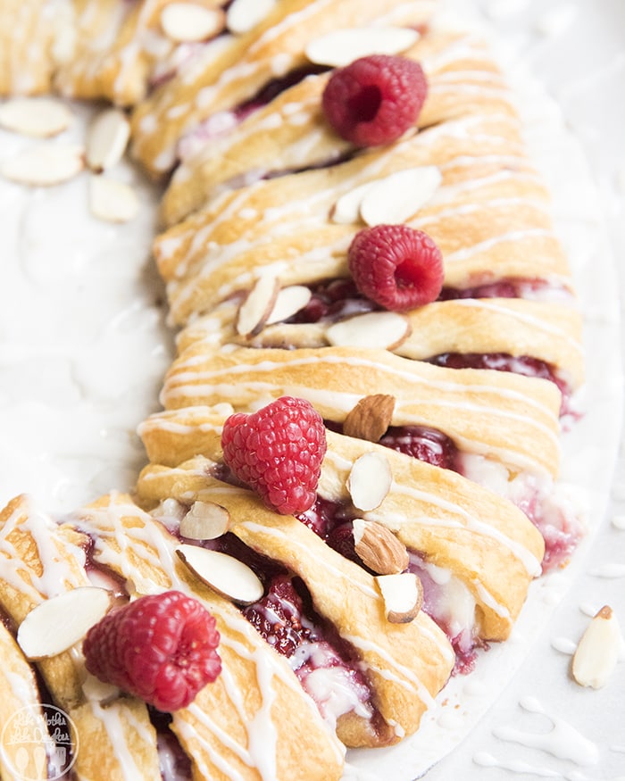 A close up of a raspberry cream cheese crescent ring with almond slices and raspberries on top.