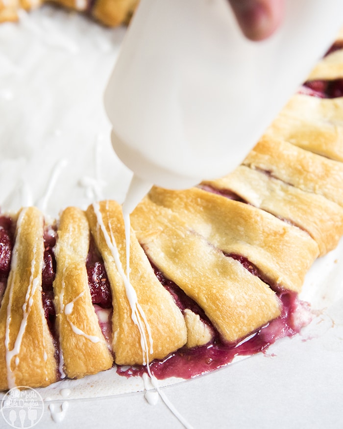 Icing being drizzled on a raspberry crescent ring pastry. 