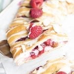 A piece of raspberry cream pastry on a spatula with a fresh raspberry on top.