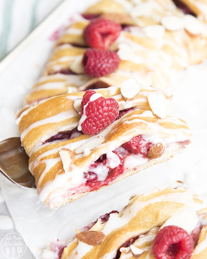 A piece of raspberry cream pastry on a spatula with a fresh raspberry on top.