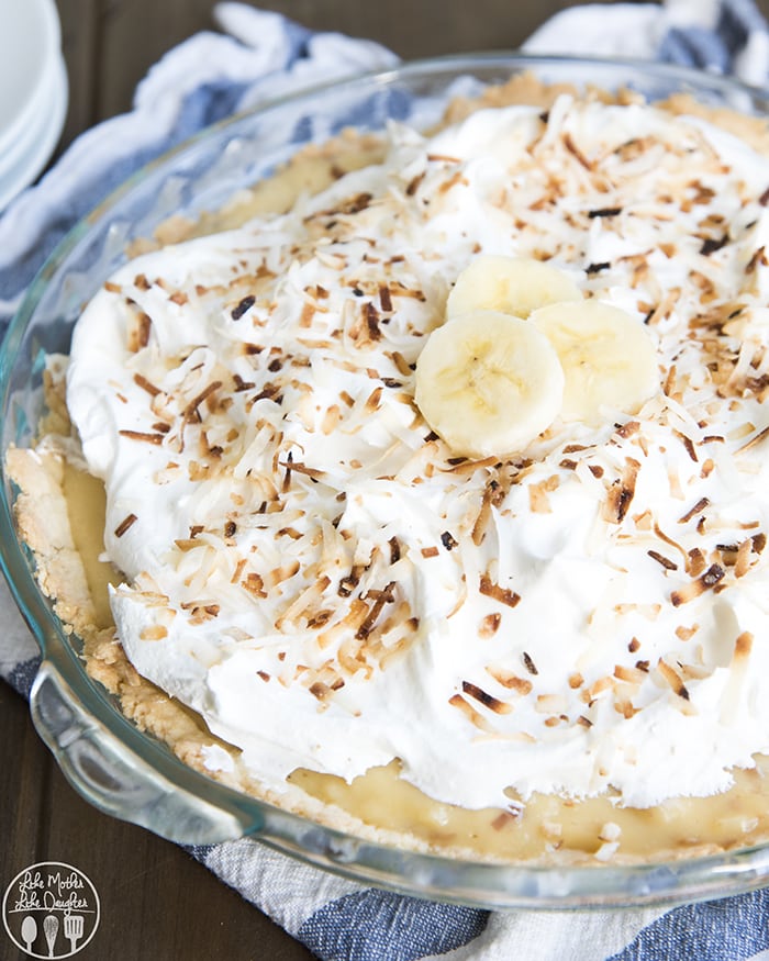A coconut and banana cream pie topped with whipped cream and toasted coconut, and three banana slices.