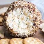 Close up image of a classic cheese ball rolled in nuts with crackers on a plate.