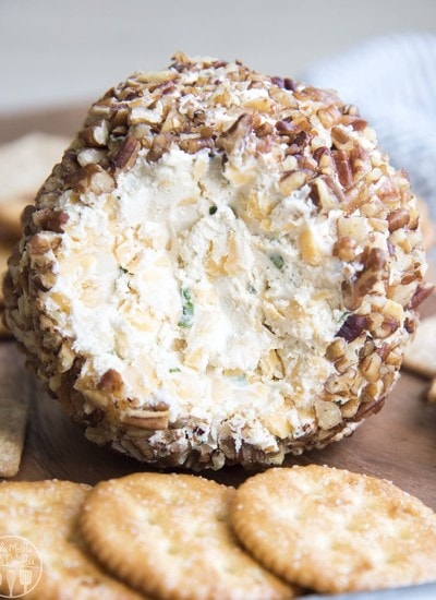 Close up image of a classic cheese ball rolled in nuts with crackers on a plate.