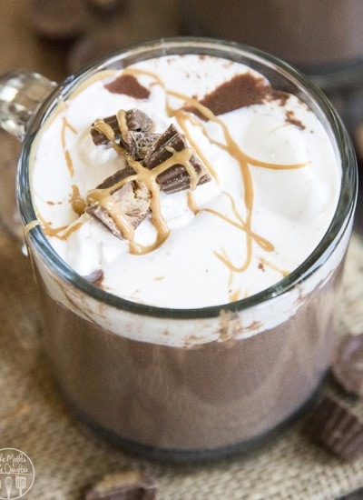 A mug of chocolate peanut butter hot chocolate topped with whipped cream and chopped peanut butter cups.
