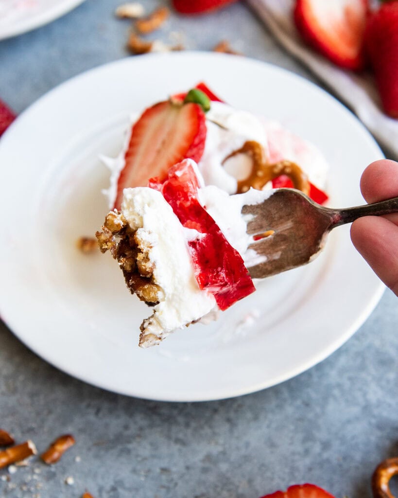 A forkful of strawberry jello salad with a pretzel crust, cheesecake filling, and jello on top.