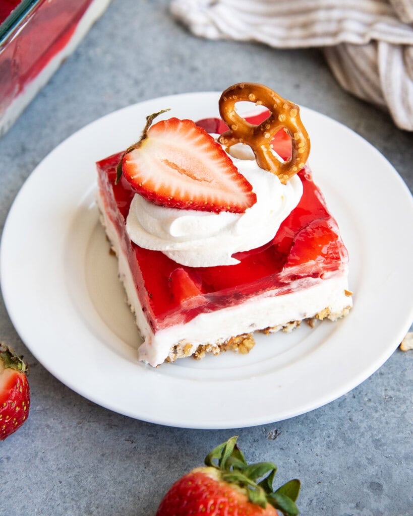 A plate of strawberry pretzel salad with a layer of pretzel crust, cheesecake filling, strawberry jello, annd whipped cream on top.