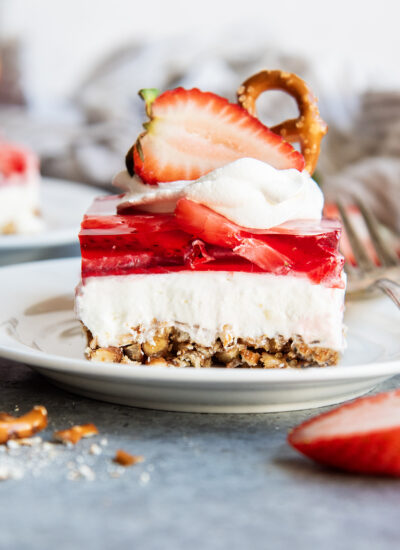 A plate of strawberry pretzel salad with a layer of pretzel crust, cheesecake filling, strawberry jello, annd whipped cream on top.