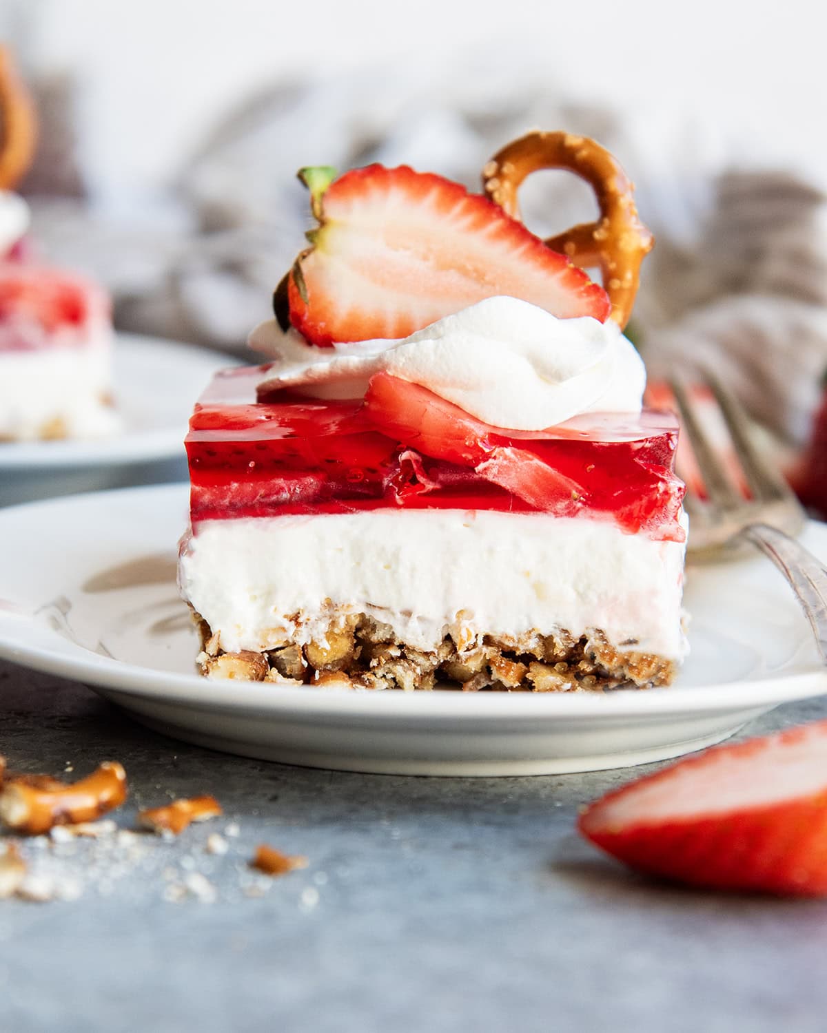 A plate of strawberry pretzel salad with a layer of pretzel crust, cheesecake filling, strawberry jello, annd whipped cream on top.