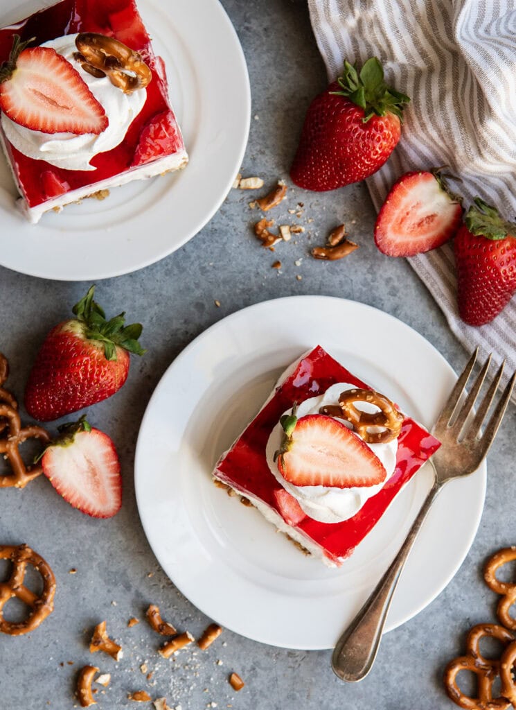 An above view of two plates of strawberry pretzel jello with whipped cream and a fresh strawberry on top.