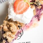 A piece of berry custard pie topped with whipped cream and half a strawberry.