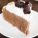 A slice of chocolate french silk pie with whipped cream and chocolate curls on top.
