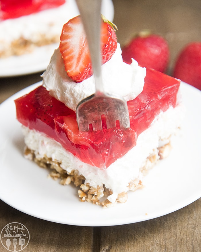 A slice of pretzel jello salad topped with whipped cream and half a strawberry on top. 