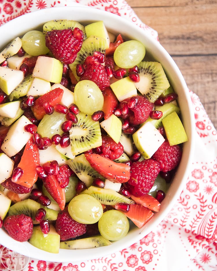 An overhead bowl of fruit salad with kiwi, grapes, apples, strawberries, raspberries, and pomegranate seeds.