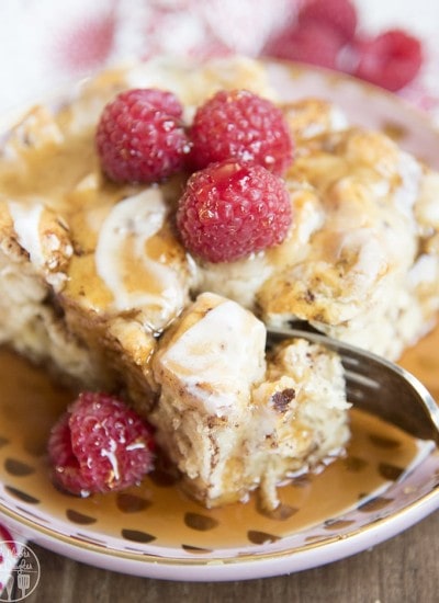A plate of cinnamon roll french toast casserole topped with raspberries.