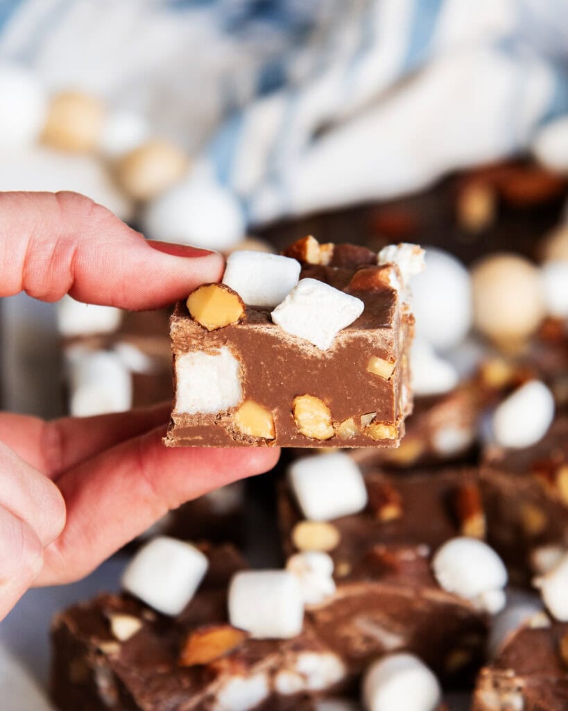 A hand holding a piece of fudge full of mini marshmallows and almonds.