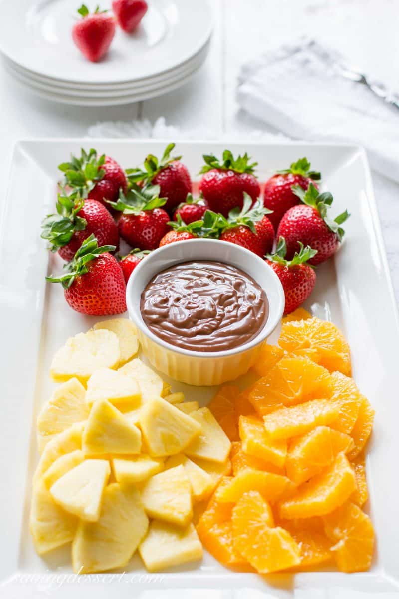 A plate of fruit and a bowl of chocolate caramel fruit dip in the middle.