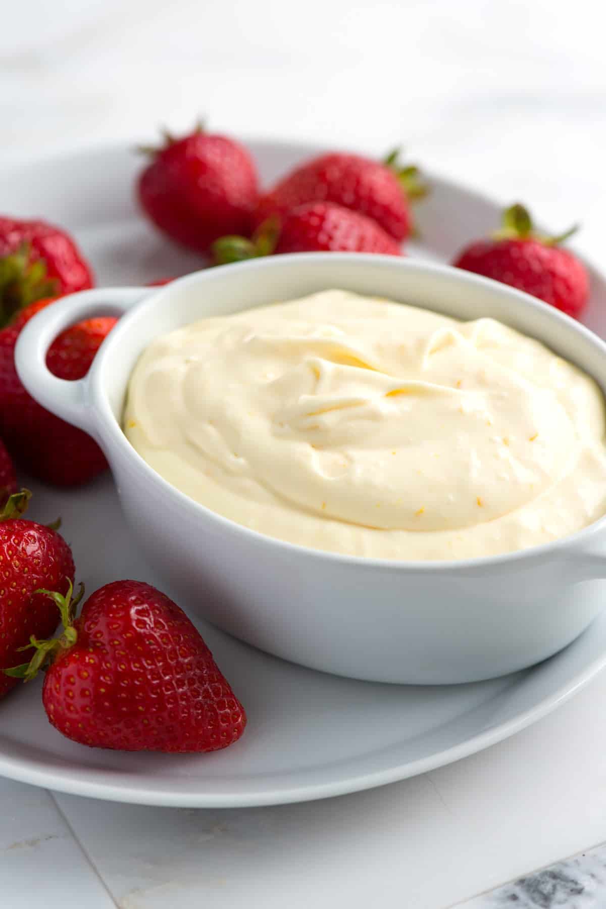 A bowl of a pudding fruit dip with strawberries around it.