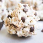A smores popcorn ball with marshmallows, chocolate chips, and golden graham cereal.