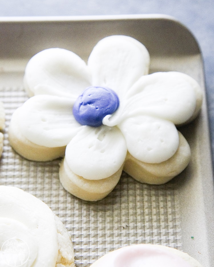 A flower shaped sugar ocokie with purple and white frosting.