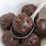 Close up image of chocolate cookie dough balls on a spoon in a white bowl.
