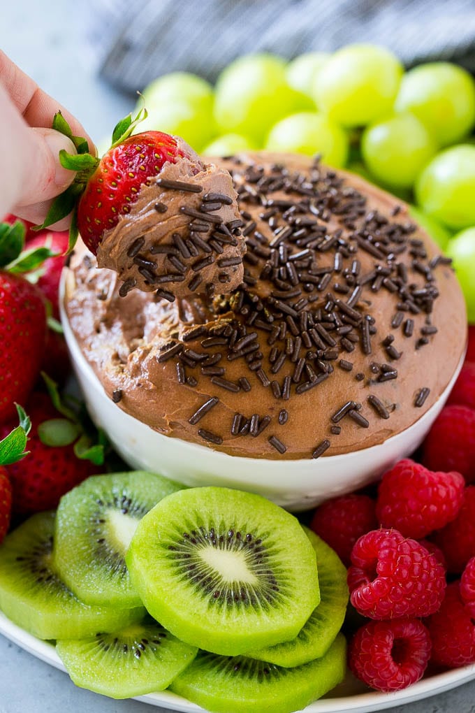 A chocolate fruit dip in a bowl, with a hand dipping a strawberry in it.