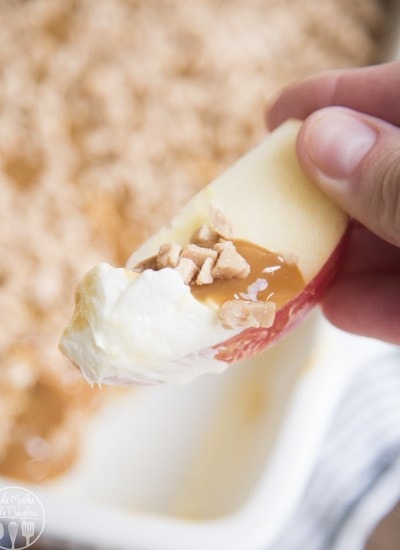 Close up image of cream cheese caramel apple dip on an apple slice held by a hand.