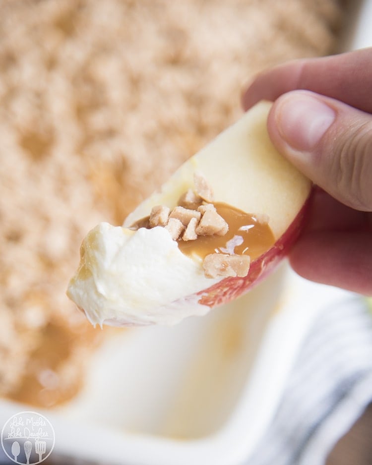 Close up image of cream cheese caramel apple dip on an apple slice held by a hand.