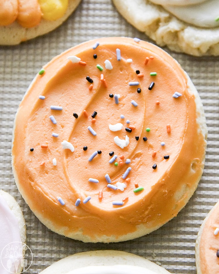 An orange frosted cookie with Halloween sprinkles on top.