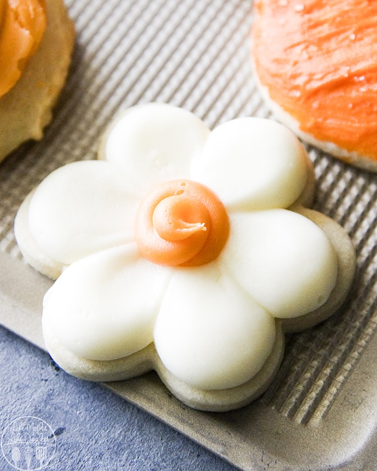 A flower shaped sugar cookie that is frosted and topped with an orange center.